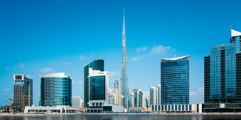 A clear daytime view of Dubai’s iconic skyline with the towering Burj Khalifa surrounded by modern skyscrapers reflected on calm waters — a stunning showcase of the top attractions in Dubai, including architectural marvels, luxury hotels, shopping hubs, and breathtaking urban views.