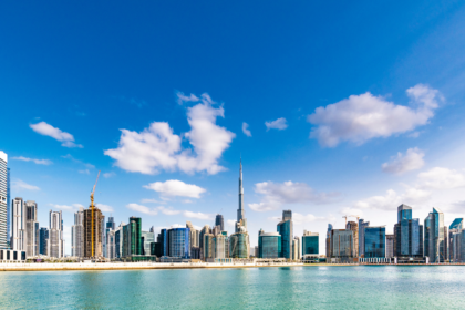 A panoramic daytime view of Dubai’s iconic skyline with the Burj Khalifa rising tall among modern skyscrapers, reflecting over clear blue waters under a bright sky — an essential highlight on any Dubai travel checklist, covering must-see landmarks, urban attractions, and unforgettable cityscape views.