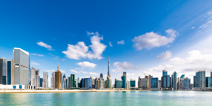 A panoramic daytime view of Dubai’s iconic skyline with the Burj Khalifa rising tall among modern skyscrapers, reflecting over clear blue waters under a bright sky — an essential highlight on any Dubai travel checklist, covering must-see landmarks, urban attractions, and unforgettable cityscape views.