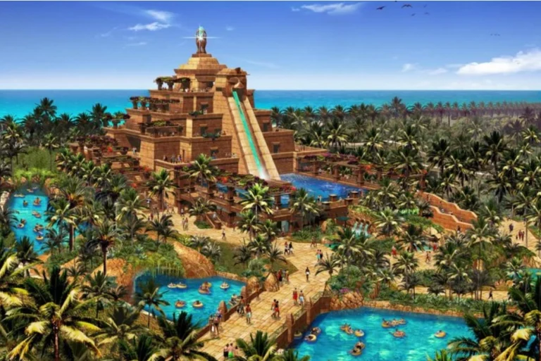 Vibrant aerial view of Atlantis Aquaventure Waterpark in Dubai, featuring the iconic pyramid-like structure of the Leap of Faith waterslide, surrounded by tropical palm trees, lazy rivers, splash pools, and visitors enjoying various water attractions under a clear blue sky.