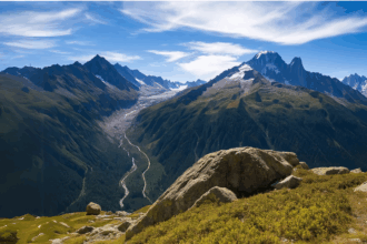 Scenic mountain valley with lush green slopes, a winding trail, and snow-capped peaks under a clear blue sky, symbolizing nature exploration and experiences similar to Dubai hiking adventures in mountainous desert surroundings.