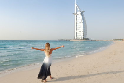 Woman in sleeveless dress walking on Dubai beach near Burj Al Arab showing how to dress in Dubai at the beach. the background shows burj al arab at a distance and the girl is enjoying the beach during the day time.